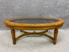 An early 20th century coffee table with an oval glass top inset into a shaped and moulded burr