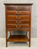 An Edwardian mahogany music cabinet with a moulded cornice above five drawers with fold down fronts,