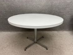 A mid-century white circular dining table with a composite laminated top on a four footed polished