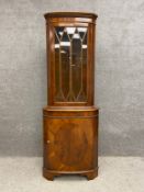 A 19th century style yew wood bow fronted corner display cabinet with a dentil moulded cornice