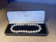 A necklace composed of a single row of faux pearls with a gold coloured clasp, in a box stamped