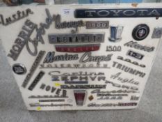 A COLLECTION OF VINTAGE CAR BADGES MOUNTED ON A WOODEN BOARD