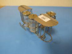 A NOVELTY WIRE WORK CRUET AND EGG CUP STAND IN THE FORM OF A BI PLANE , EGG CUP HAS NO BASE