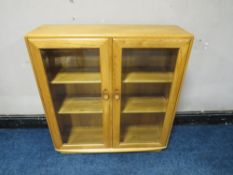 AN ERCOL LIGHT ELM GLAZED TWO DOOR BOOKCASE, H 98 cm, W 91 cm