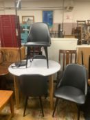 A modern circular white dining table with four black chairs and standard lamp