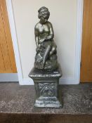 A GARDEN STATUE ON PLINTH OF A FEMALE FIGURE SEATED ON A ROCK, H 94 cm