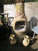A terracotta chimenea with two ornamental jugs