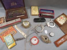 A tray of assorted collectables to include vintage handcuffs, playing cards, cased instrument set,