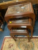 A carved hardwood eastern nest of three tables with glass tops