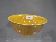 A Chinese style small footed bowl in mustard yellow with indistinct decoration of winged figures