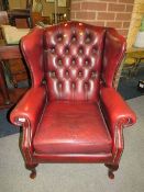 An oxblood red leather chesterfield style wing back armchair