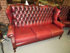 An oxblood red leather chesterfield style three seater wing back sofa