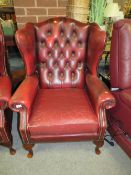An oxblood red leather chesterfield style wing back armchair