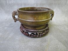 AN ORIENTAL TWIN HANDLED BRONZE CENSOR, with six character mark to the base, on a hardwood stand,