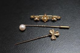 A HALLMARKED 9 CARAT GOLD SHAMROCK STICK PIN, together with a pearl example and an unmarked yellow