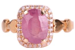 A ruby and cubic zirconia cluster ring; the oval mixed cut ruby in four claw mount above a border of