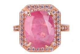 A ruby and cubic zirconia cluster ring; the oval cushion cut ruby in four claw mount above a border 