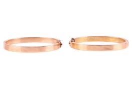 A pair of hinged bangles, of plain flat hollow bands, finished with concealed tongue clasps and safe