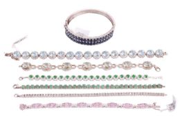 A collection of gem-set bracelets comprising a white metal hinged bangle set with glass filled sapph
