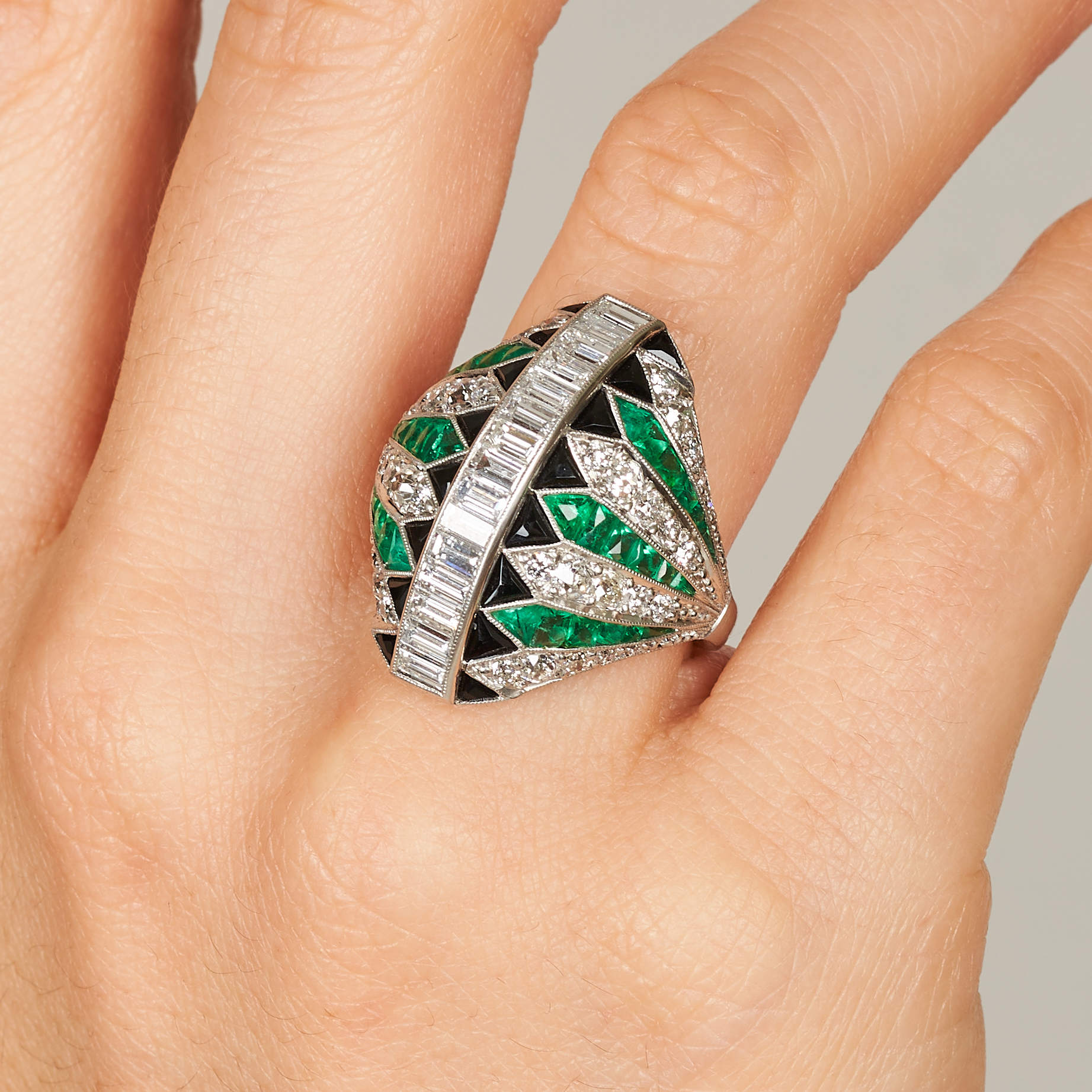 A FINE ART DECO DIAMOND, EMERALD AND ONYX DRESS RING of bombe design, set with a row of baguette ...
