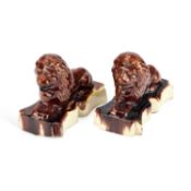 A PAIR OF VICTORIAN TREACLE-GLAZED POTTERY MODELS OF RECUMBENT LIONS