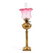 A BRASS COLUMNAR OIL LAMP WITH RUBY TINTED GLASS SHADE