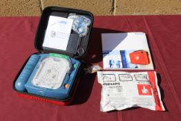 A Philips HeartStart defibrillator in hard carry case, with owners manual, and a smart pad cartridge