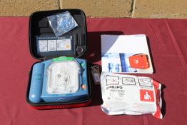A Philips HeartStart defibrillator in hard carry case, with owners manual, and a smart pad cartridge