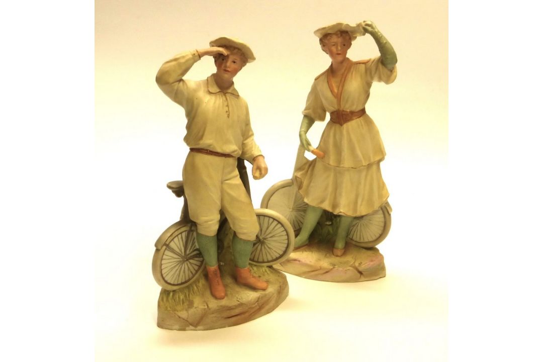 A pair of figurines by Gebruder Heubach. 'Bisque' figurines of a boy and girl bicycle riders, c.