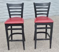 2 x Bar Stools Featuring a Black Finish With Red Cushioned Seat, Foot Support and Ladder Back -