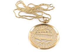 YELLOW METAL PIERCED PENDANT depicting sun over The Parthenon within Greek key border, on yellow