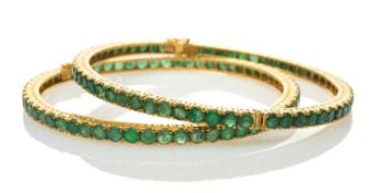 TWO SIMILAR YELLOW METAL BELIEVED EMERALD SET HINGED BANGLES, one stamped '22K' the other stamped '