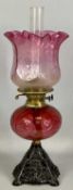 19TH CENTURY OIL LAMP with pierced cast iron base, moulded cranberry glass reservoir, twin