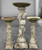 THREE CAST STONE BIRD BATHS, larger with cupid/urchin column, 95 (h) x 37cms (w), smaller two with