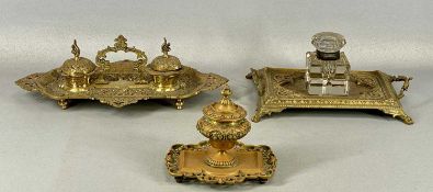 THREE VICTORIAN CAST BRASS DESK STANDS, one having twin inkwells and centre carry handle, 38cms (h),