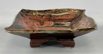 SQUARE STONEWARE DISH, raised on four feet with tenmoku glaze, impressed mark, 30cms (w) Provenance: