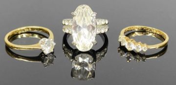 THREE DRESS RINGS, one white metal set with large oval clear stone, one yellow metal set with five