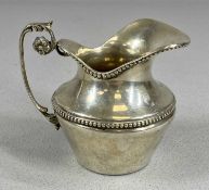 CONTINENTAL WHITE METAL CREAM JUG of circular form having a bead border, ornate handle with floral