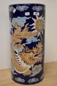 A Chinese cylindrical stick or umbrella stand, decorated with a dragon design against the cobalt