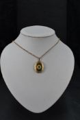 A 9ct gold oval locket having a central blue stone with engraved decoration on a 9ct gold belcher