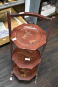 A vintage three tiered wooden cake stand, having gilt painted scenes to each tier.