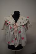 A 1950s cotton bed jacket, having bright rose pattern, quilted yolk and ribbon to fasten.
