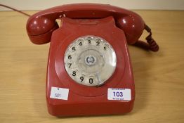 A vintage red rotary telephone.