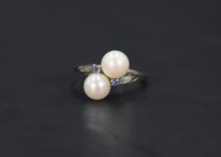 A cultured pearl crossover ring with sapphire chip set shoulders on a white metal loop stamped