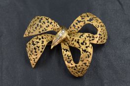 A large 18ct gold brooch in the form of a bow having a damask pattern with diamond chips to the