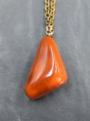 A large amber style pendant of triangular form on a yellow metal chain, 30.7g