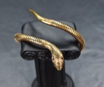 A 9ct gold flexible snake bangle, with ruby set eyes and decorative engraving to the head and