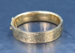 A 9ct gold hinged bangle having engraved scroll decoration, safety chain broken, inner diameter 62mm