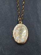 A yellow metal oval locket having a decorative floral design engraving on a 9ct gold rolo chain, 7.