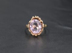 An oval amethyst ring having a four claw setting in decorative moulded surround on a yellow metal
